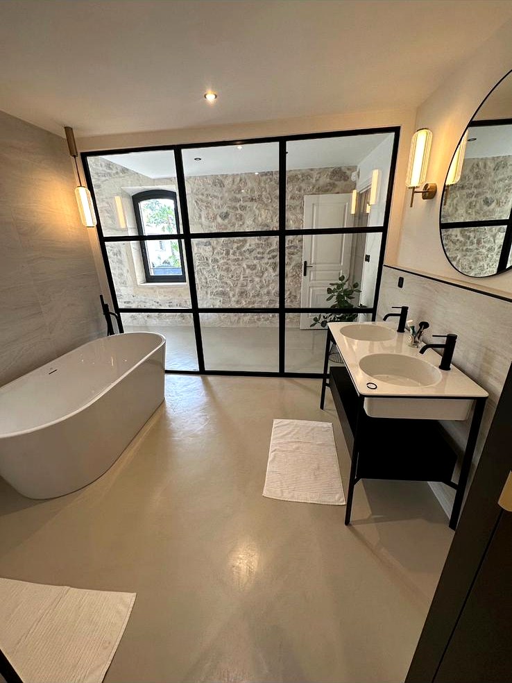 Salle de bain haut de gamme avec baignoire îlot et grande verrière noire réalisée par Ô Douce