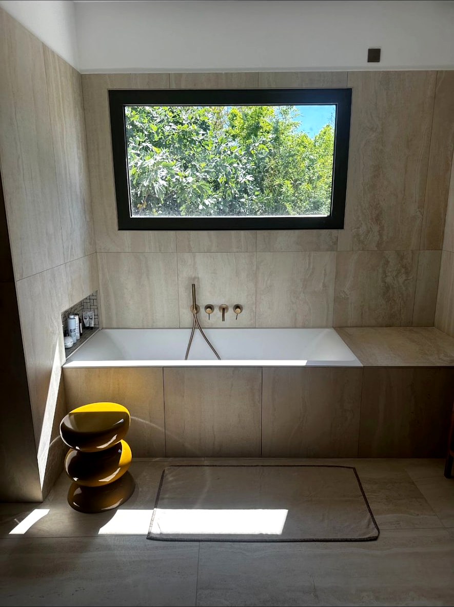 Baignoire encastrée sous une fenêtre dans une salle de bain en travertin dans l'Hérault