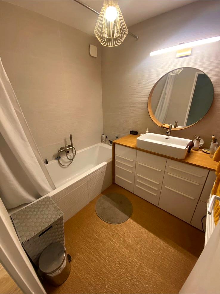 Meuble de salle de bain avec plan en bois, vasque à poser blanche et grand miroir rond